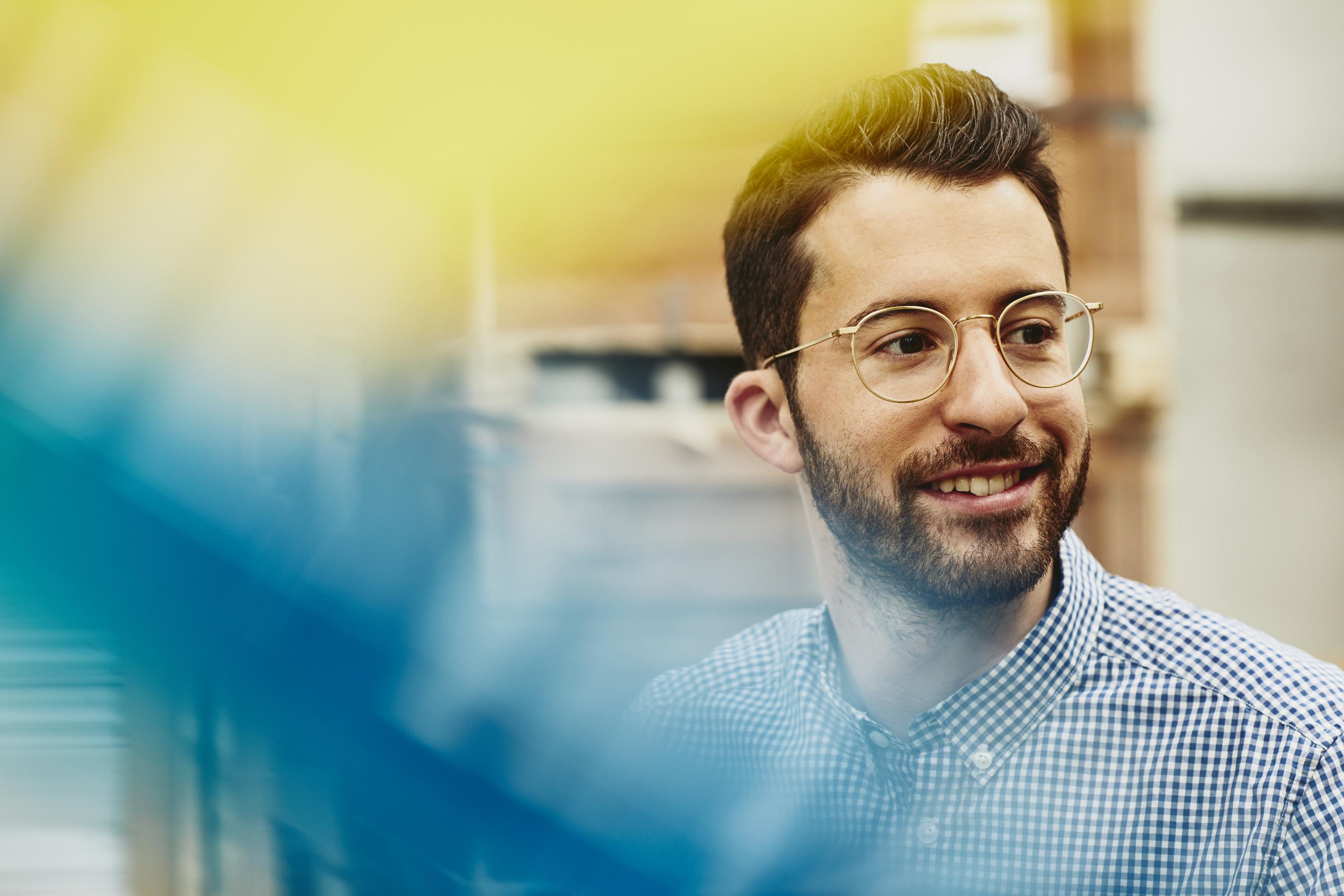 Male caucasian worker in logistics environment. Wearing glasses. Checkered shirt. Groomed beard and moustache. Primary color blue. Secondary color yellow.