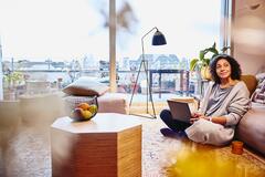 Woman leaning against a couch, sitting on the floor, with laptop on her lap