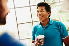 Smiling man holding a coffee cup having a chat with someone.