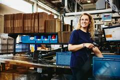 Smiling woman standing next to conveyer belt holding a scanner