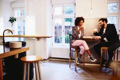 Woman and man sitting at a table with coffee. Having a conversation. Smiling.