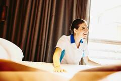 Smiling woman making a bed in a hotel room.