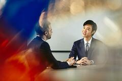 Two business men talking in a meeting, sitting, tablet, whiteboard in the background.