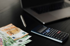 Banknoty euro leżą obok kalkulatora i laptopa 