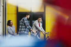 Group of colleagues (two males, one female) leaving work. Bicycle. Two caucasian males. One African-American woman. Checkered shirt and striped T-shirt. Primary color red. Secondary color yellow.