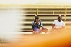Blue-collor workers during lunch break. Laughing. Female Asian and male African-American. Checkered shirt and white T-shirt. Primary color yellow/orange. Secondary color white.