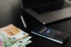 Banknoty euro leżą obok kalkulatora i laptopa 