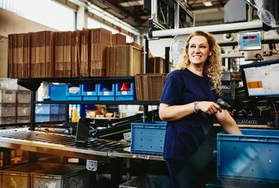 Smiling woman standing next to conveyer belt holding a scanner