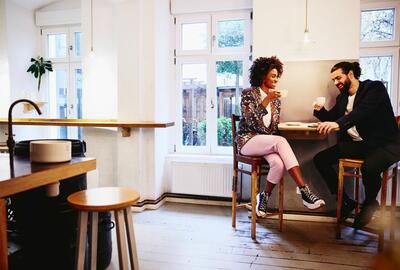 Woman and man sitting at a table with coffee. Having a conversation. Smiling.