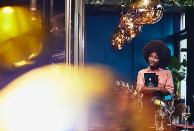 Smiling woman walking through restaurant holding menu cards.