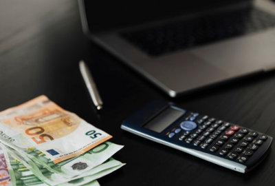 Banknoty euro leżą obok kalkulatora i laptopa 