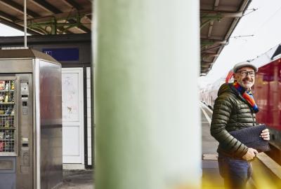 Man holding a laptop case/bag standing on a train platform.