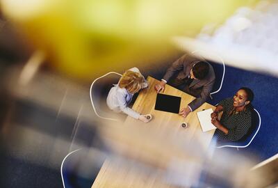 People having a meeting in an office. Woman looking up & smiling. Primary color: yellow.