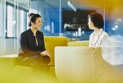 Two women talking and smiling in an office. Japan. Primary color: yellow.