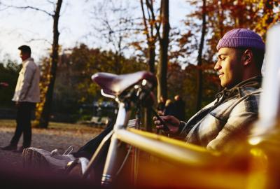 Man sitting on a bench with his bike next to him, looking at his phone.