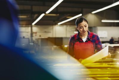 Female operator reading from paper. Factory. Tech environment. Asian woman. Primary color red. Secondary colors blue and yellow.