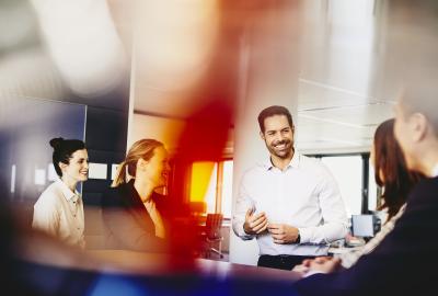 Business men and women in an office having a meeting. Primary color: red.