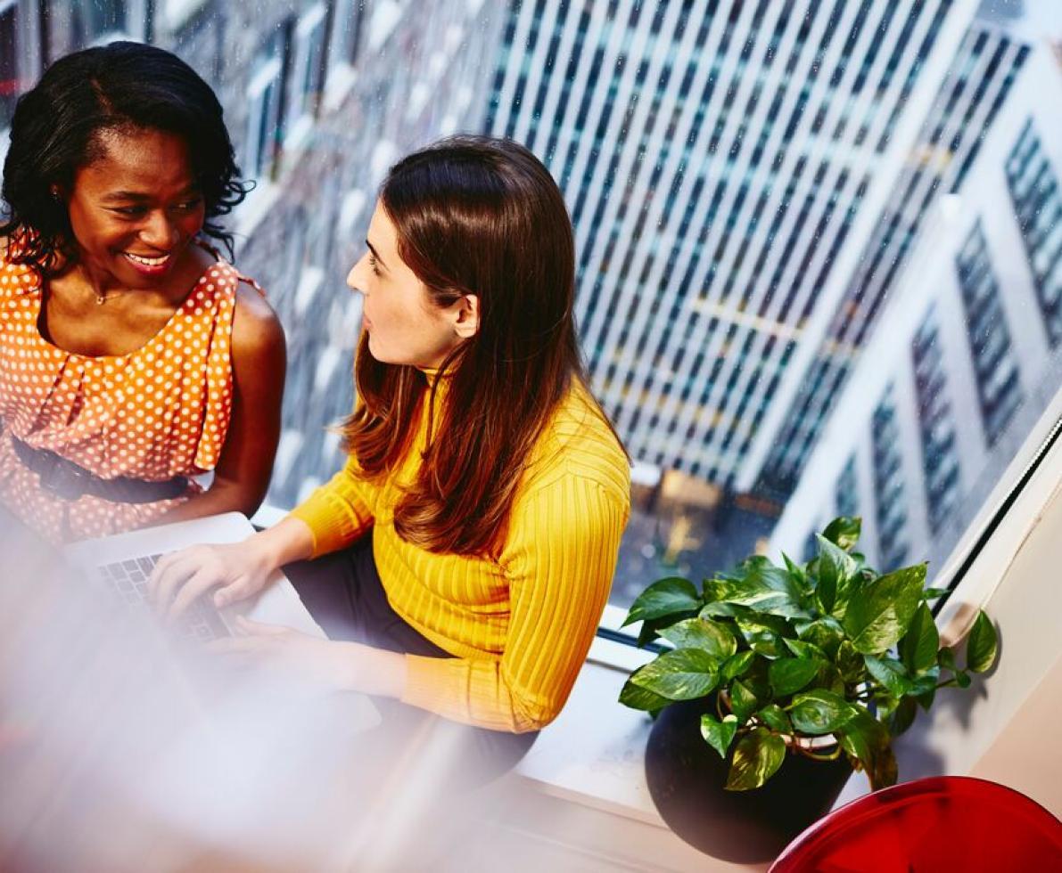 A conversation between two women of different nationalities during a meeting at work in a high office building.