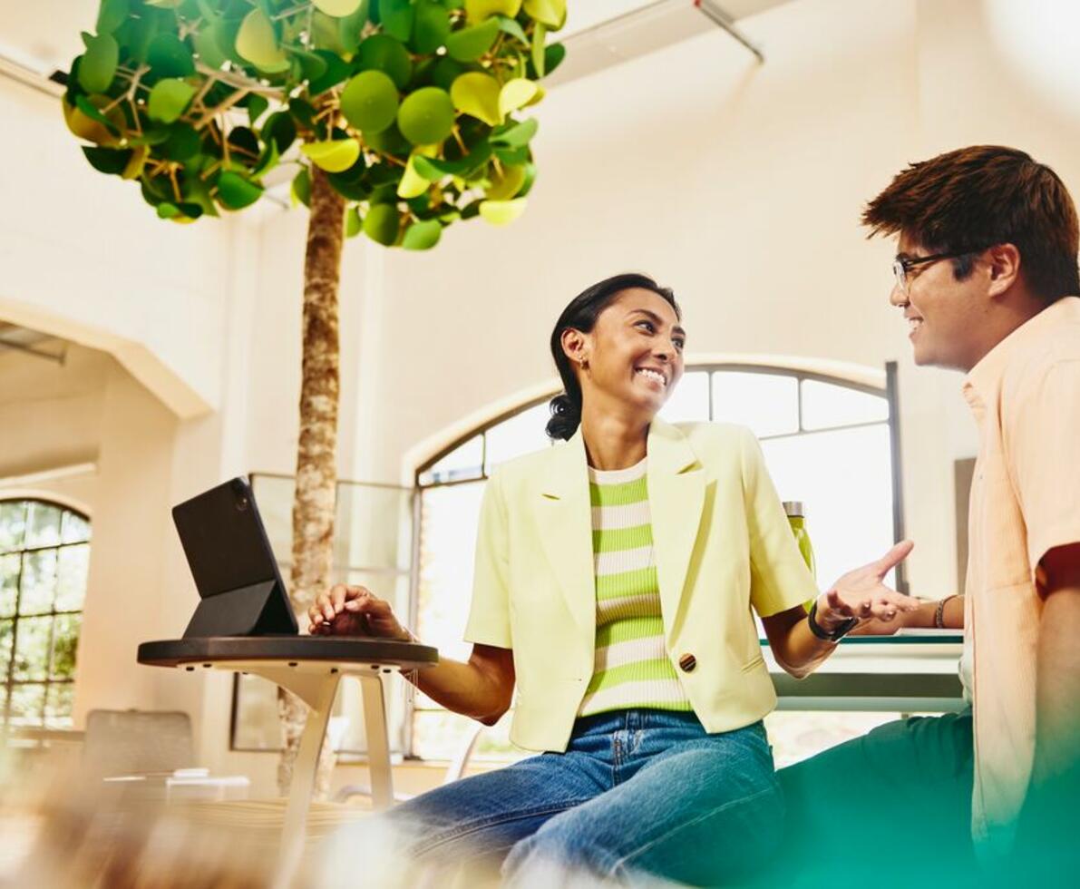Man and woman sitting at table having a chat, while woman working on a tablet.