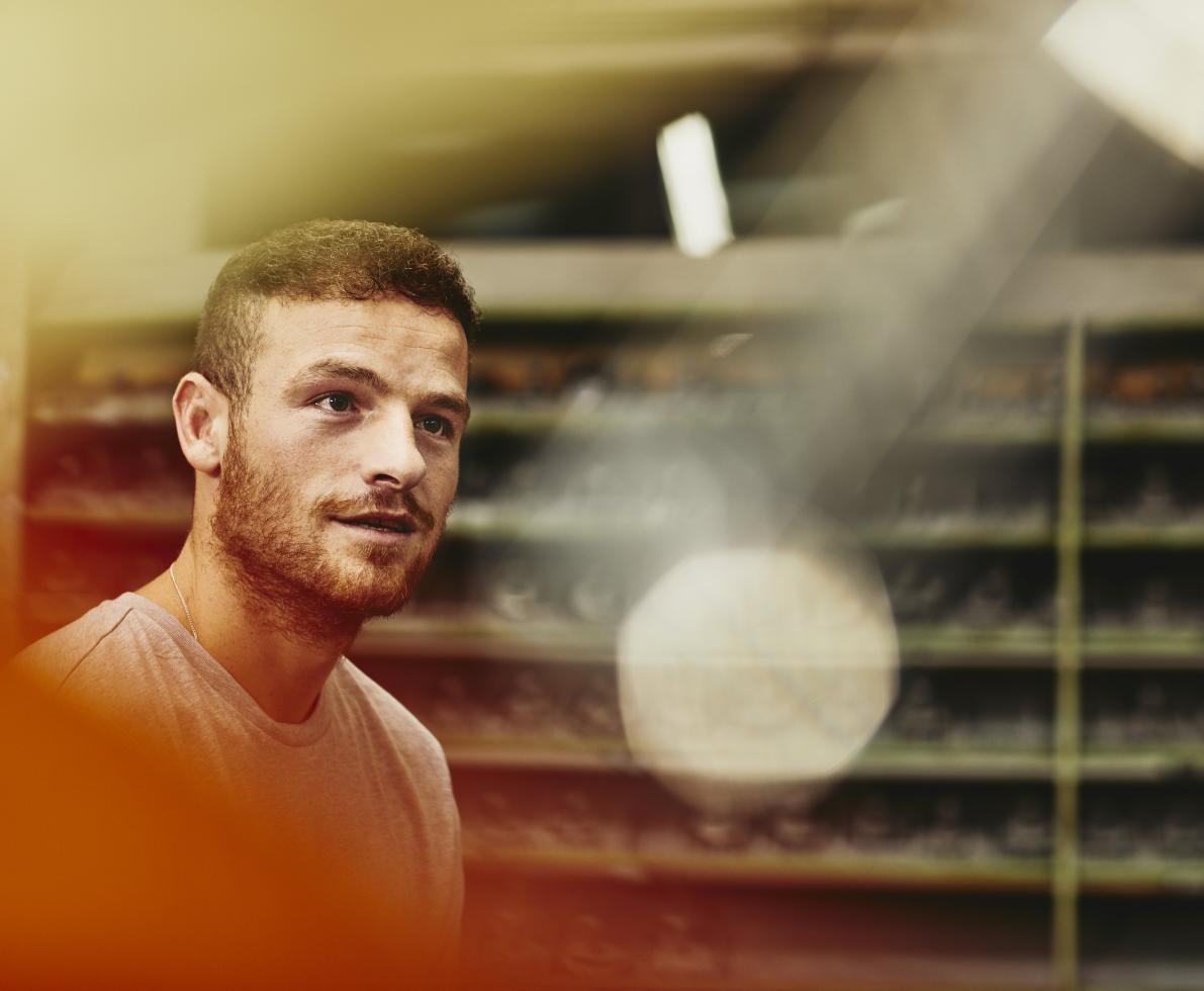 Blue-collar worker talking to someone. Looking up. Groomed beard. Caucasion man. Primary color yellow/orange.