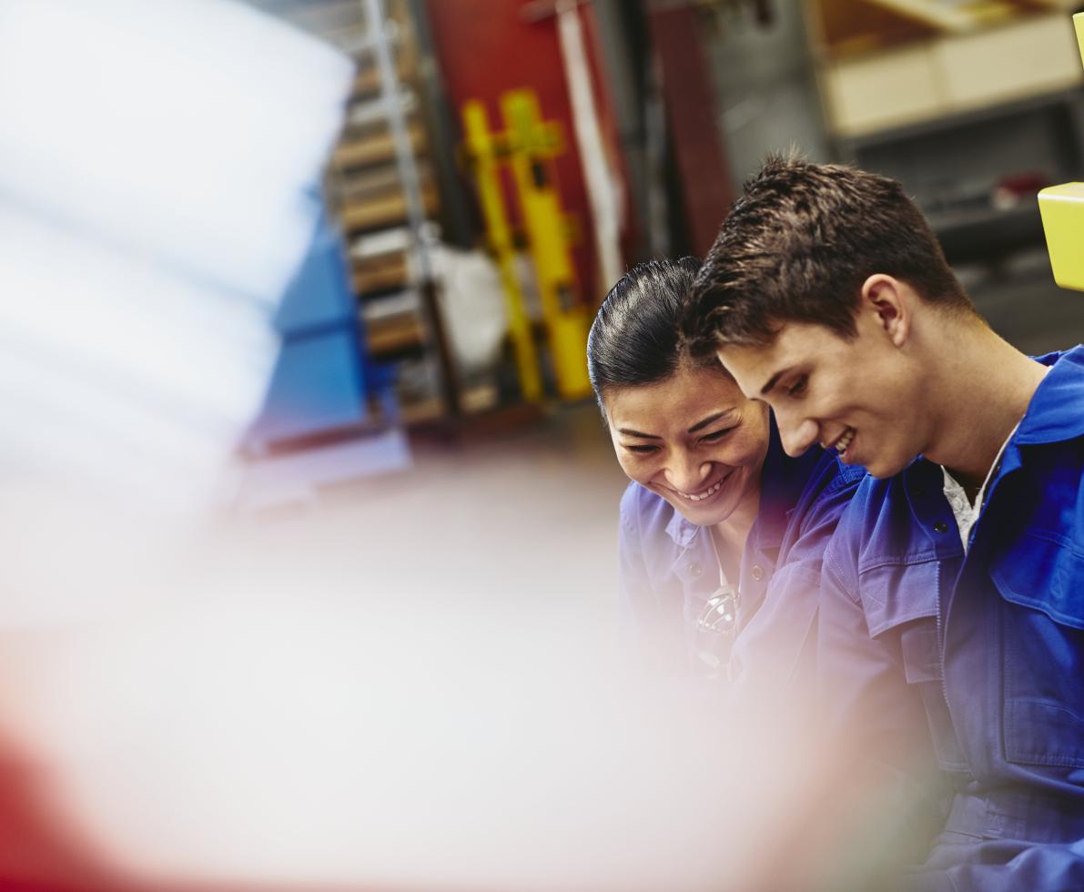 Male and female operator working together. Smiling. Caucasian man and Asian woman. Tech environment. Factory. Primary color white. Secondary color blue.