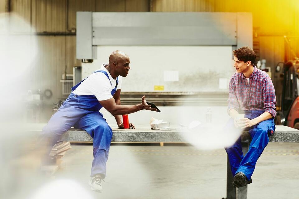 Двоє людей сидять на півстіні, дивляться на телефон і розмовляють на складі.