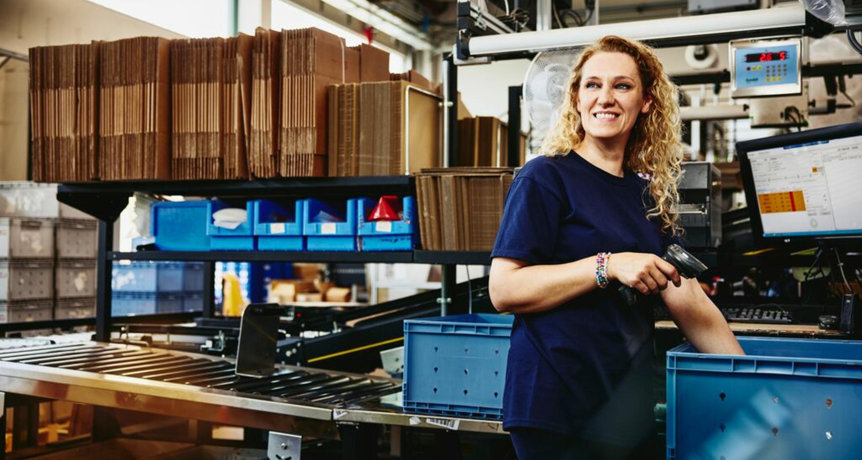 Smiling woman standing next to conveyer belt holding a scanner